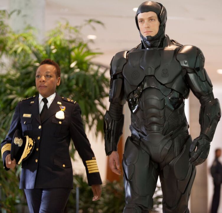 Robocop sans face covering or armour on his right hand walking next to a military person 