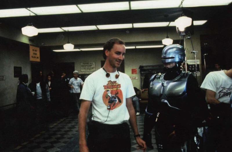 Director Fred Dekker talking to a man in a Robocop costume in a hall during production of Robocop 3