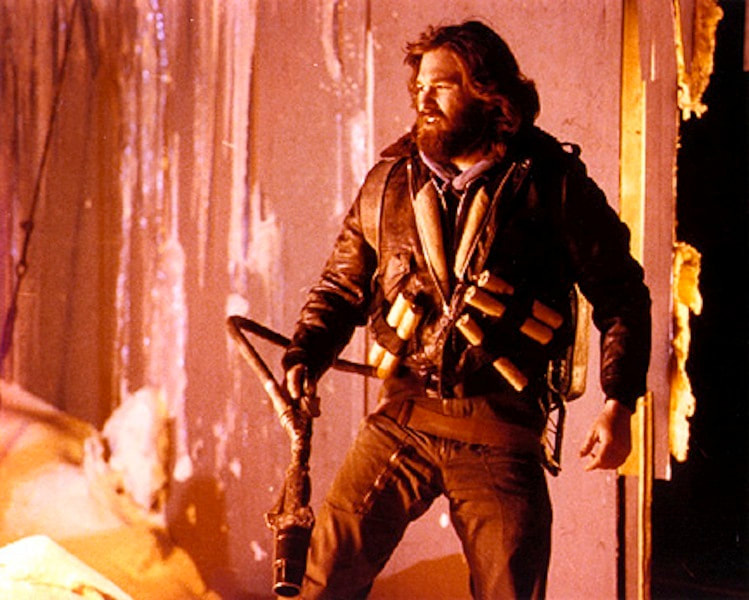 Kurt Russell wearing a flame thrower while standing back to admire his burning work in The Thing 1982